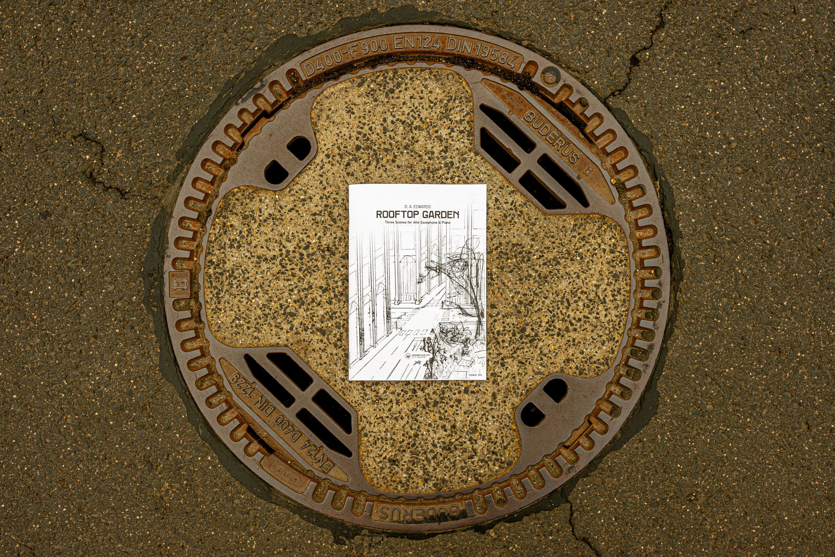 The piece portrays three scenes across shifting hours at an intersection, observed from atop the rooftop garden on a roadside city block